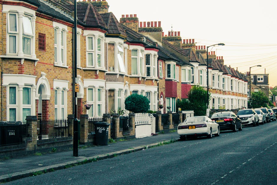 A row of terraced residential houses with brick façades, bay windows, and pitched roofs aligned along a suburban street in Haringey. The houses have small front gardens enclosed by low brick and metal