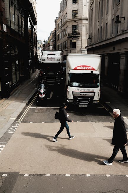 Two movers are actively engaged in a home relocation process inside the back of a delivery truck. One mover, wearing a navy blue t-shirt and black trousers with reflective strips, is standing on the t